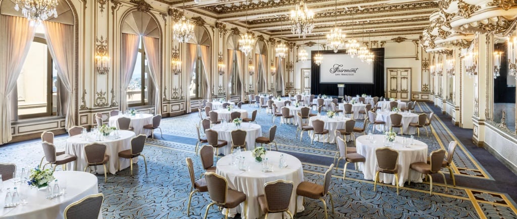 The Gold Room at The Fairmont San Francisco, set with round tables for a banquet, ornate gilded ceiling and chandeliers, and floor-to-ceiling windows